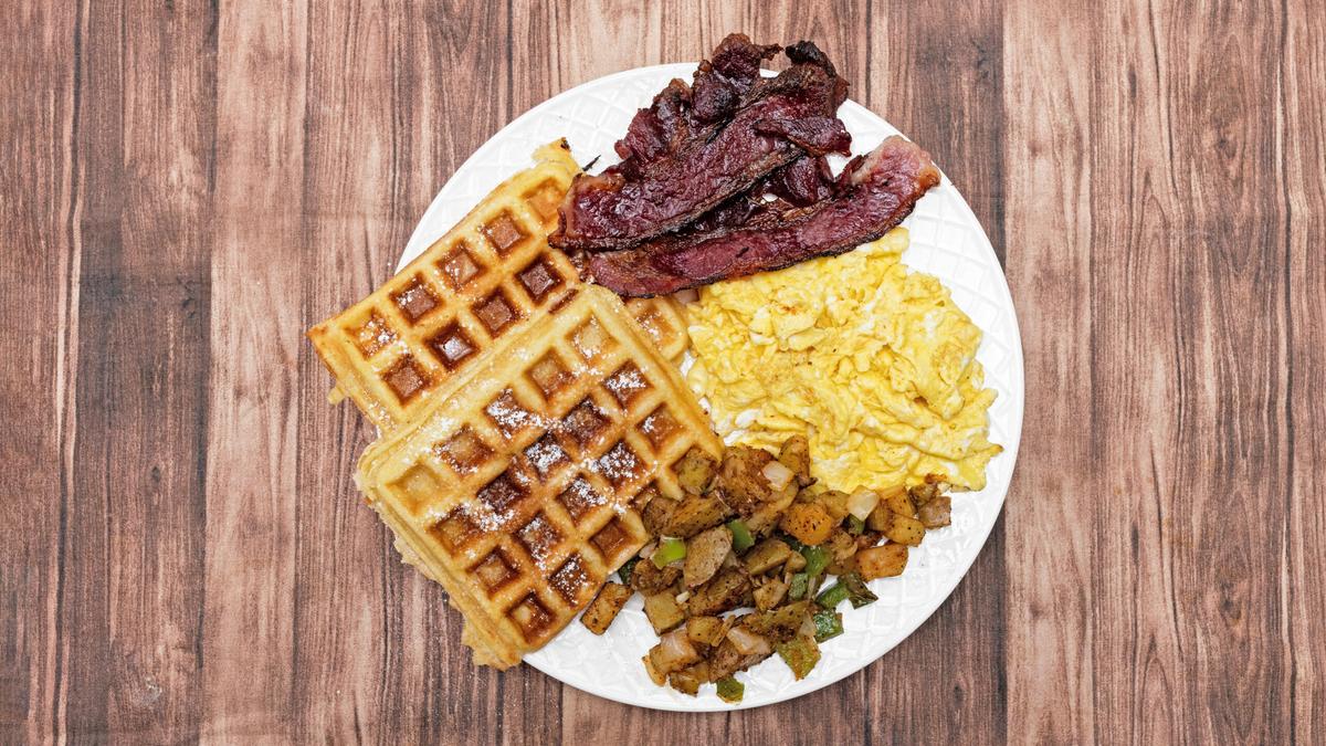 A platter of waffles, scrambled eggs, beef bacon, and home fries.