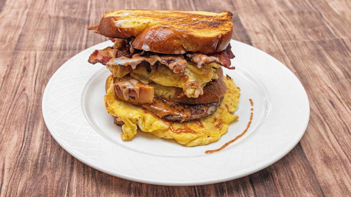 A tall three-tier sandwich stacked with two meats, double eggs, and challah bread.